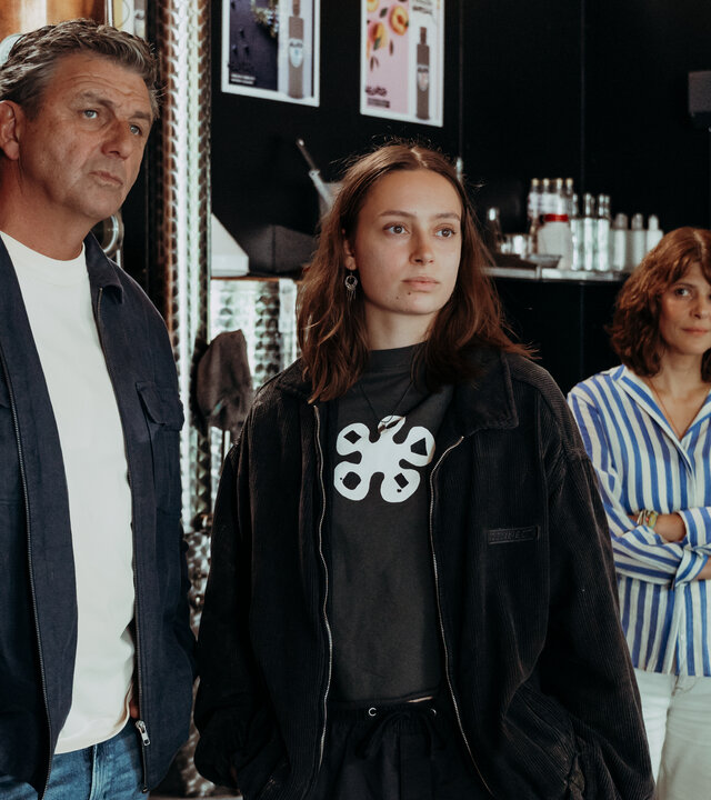 "Der Bergdoktor: Wer einmal lügt": In der Brennerei: Dr. Martin Gruber (Hans Sigl) und Lexi Helmig (Mascha Schrader) stehen nebeneinander vor einem Brennkessel und blicken nachdenklich auf etwas außerhalb des Bildausschnitts. Im Hintergrund steht Isabelle Meyer (Lale Yavaş), die Arme vor der Brust verschränkt, und beobachtet die beiden lächelnd.