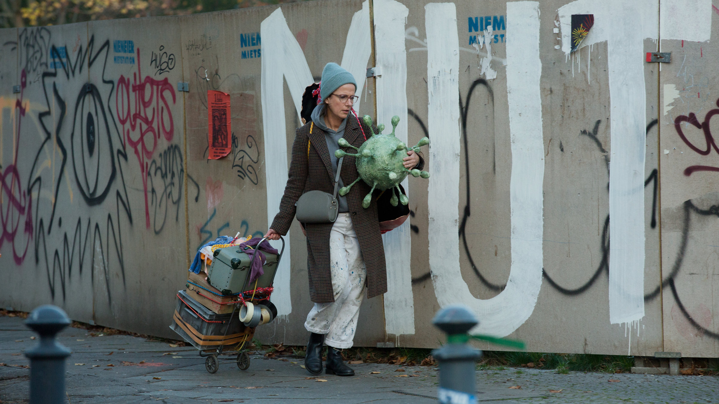 "Immer der Nase nach": Die Schaufensterdekorateurin Tanja (Claudia Michelsen) läuft mit Requisiten bepackt auf einer Straße, die an einem Bauzaun entlang führt. Der Zaun ist mit Graffiti besprüht. "Mut" ist in großen Lettern zu lesen.