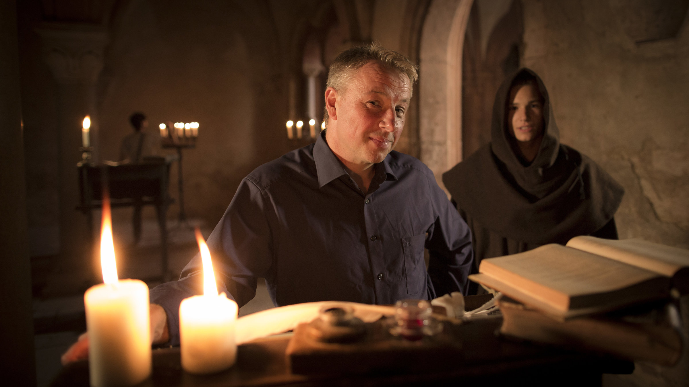 "Terra X: Zeitreise - Die Welt im Jahr 1500": Professor Wemhoff im Vordergrund am Stehpult, brennende Kerzen, Bücher und im Hintergrund ein junger Mönch.