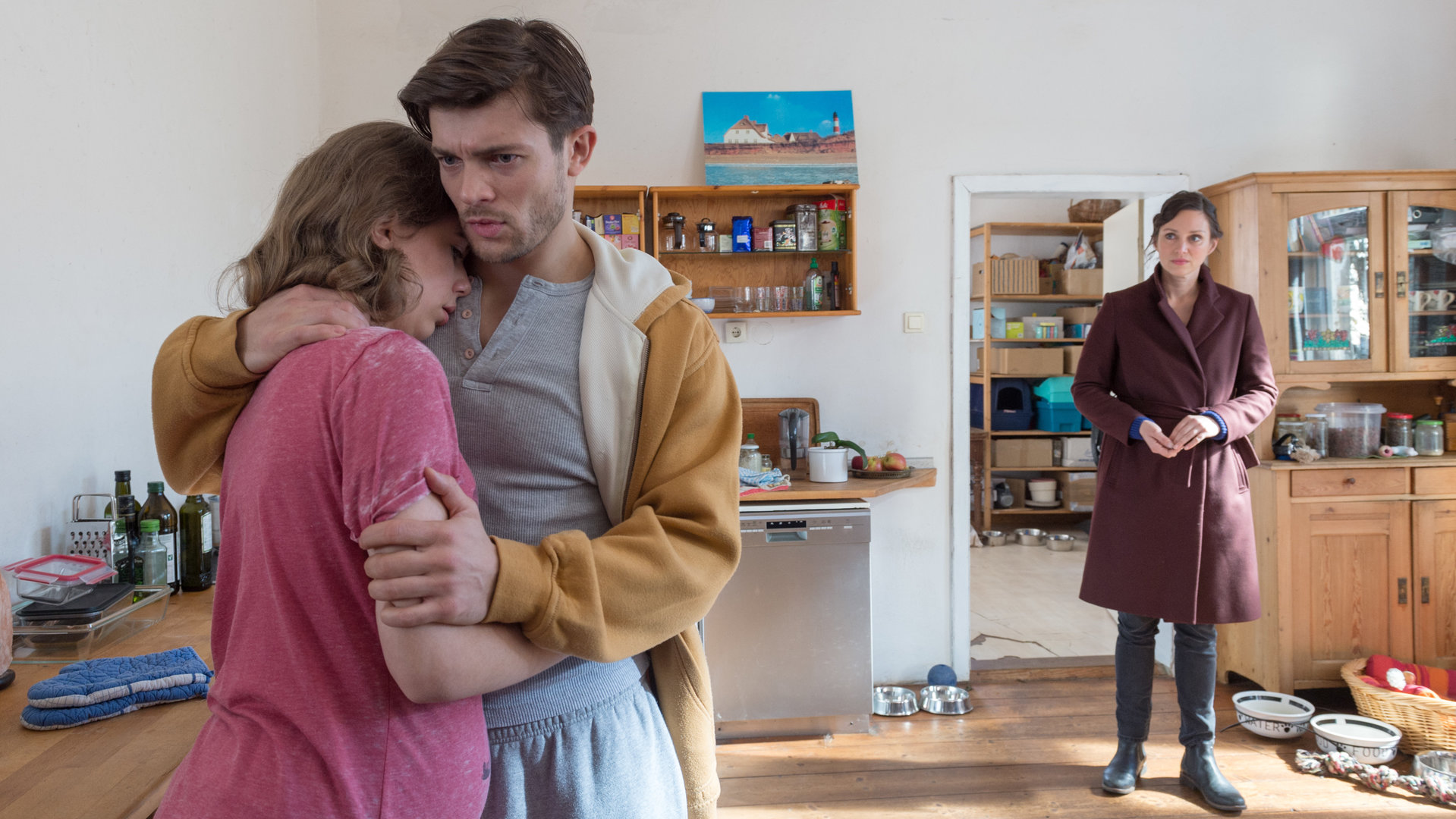 "SOKO Wismar – Taxi-Blues": Karoline Joost (Nike Fuhrmann) steht in der Wohnküche von Ella Preuss (Josepha Walter) und René Kwiatkowski (Eugen Bauder). Ella ist schwanger und wird von ihrem Freund tröstend in die Arme geschlossen.