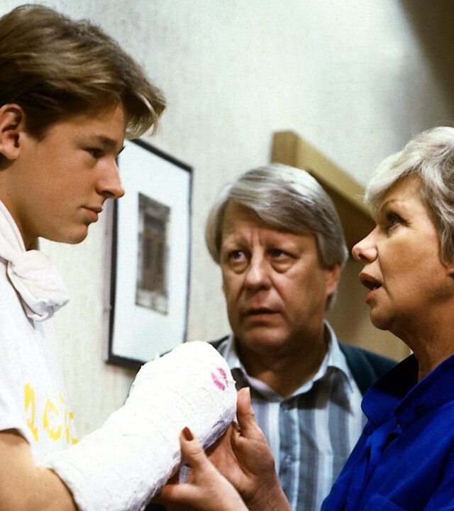 "Die Wicherts von nebenan: Hannelores Mahagoni": Andys (Hendrik Martz) Arm ist eingegipst. Hannelore (Maria Sebaldt) und Eberhard (Stefan Orlac) stehen ihm gegenüber und betrachten ihren Sohn sorgenvoll.