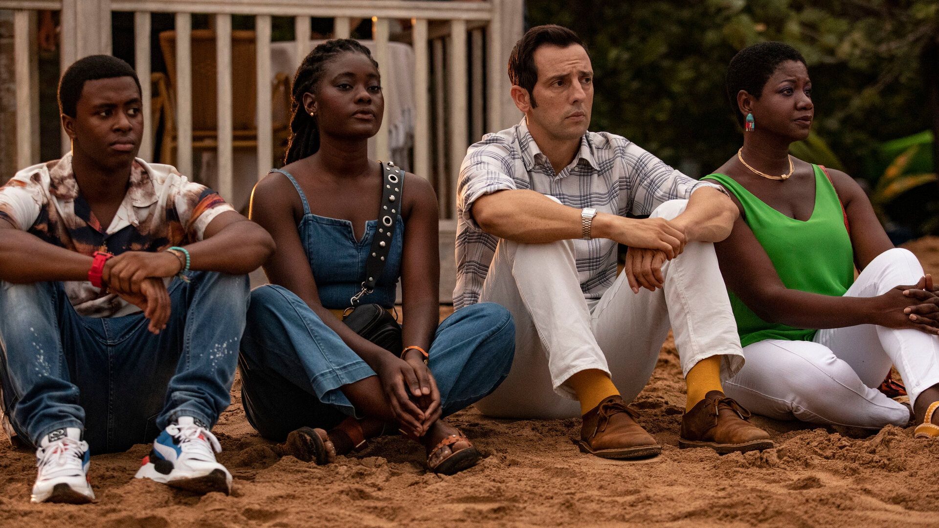 "Death in Paradise - Enttarnt": Officer Marlon Pryce (Tahj Miles), Naomi Thomas (Shantol Jackson) und Darlene Curtis (Ginny Holder) sitzen zusammen mit Detective Neville Parker (Ralf Little) am Strand und blicken in die Ferne.