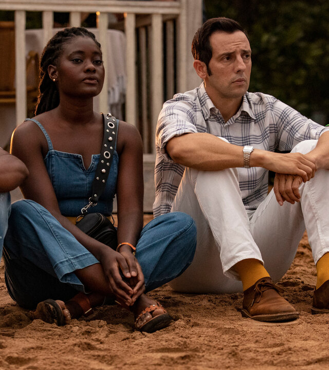 "Death in Paradise - Enttarnt": Officer Marlon Pryce (Tahj Miles), Naomi Thomas (Shantol Jackson) und Darlene Curtis (Ginny Holder) sitzen zusammen mit Detective Neville Parker (Ralf Little) am Strand und blicken in die Ferne.