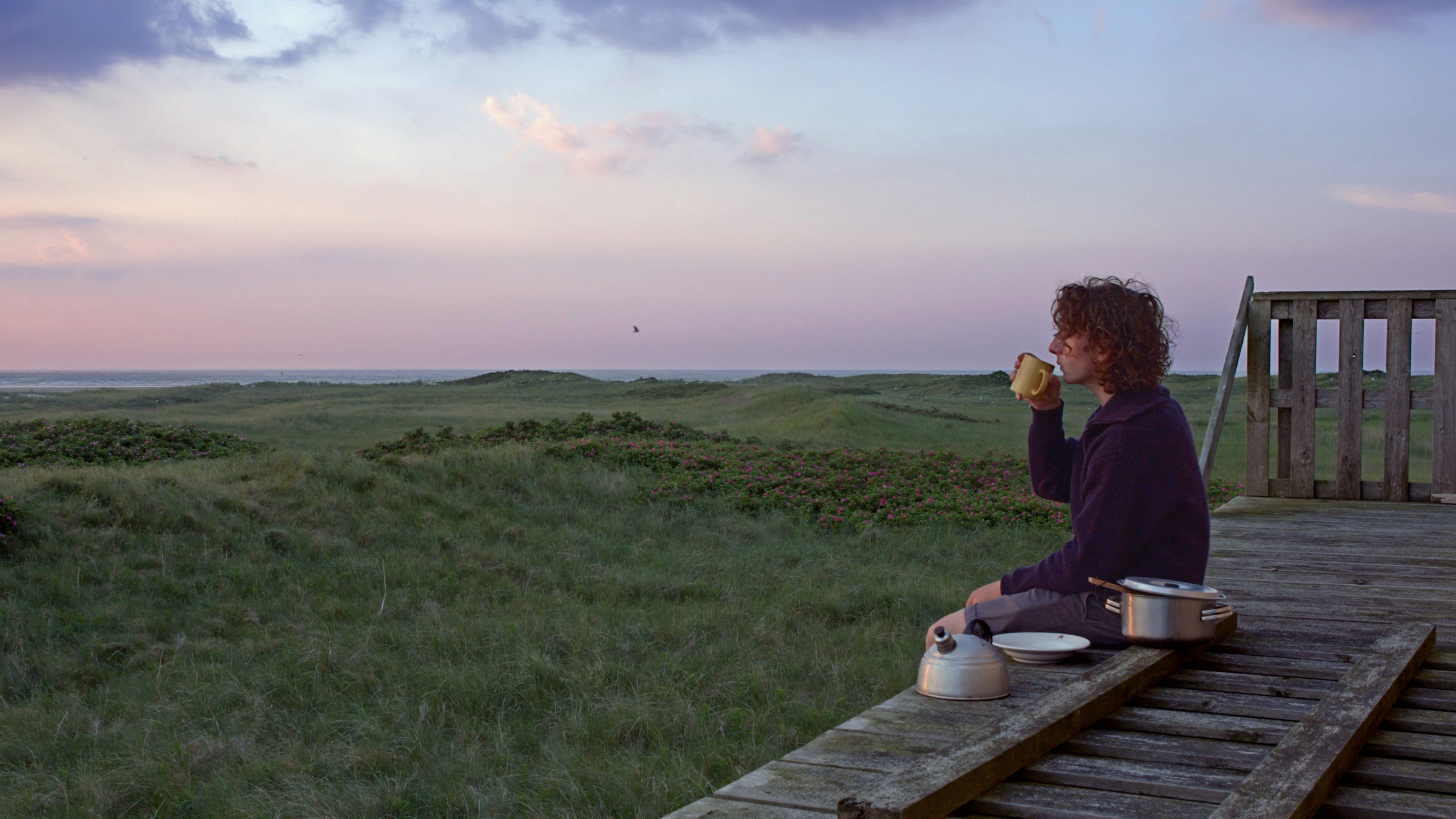 "Ab 18 - Einmannland": Junger Mann blickt sitzend in die Landschaft mit einer Teekanne neben sich.