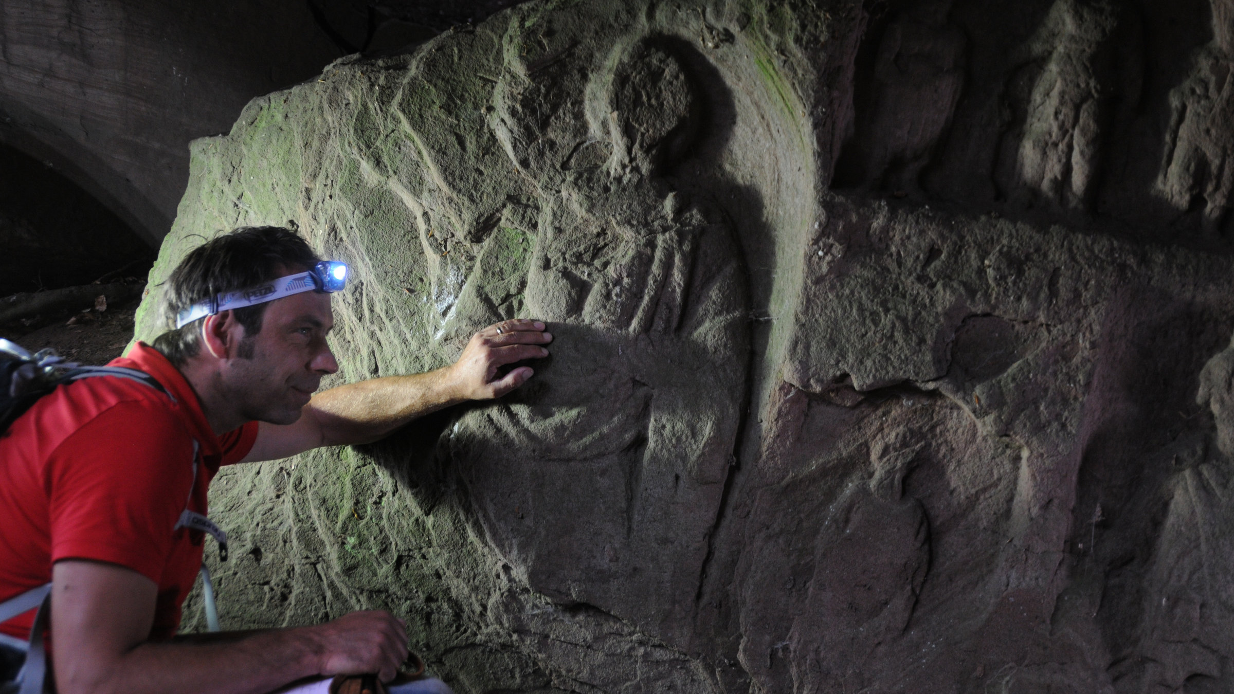 "Terra X - Magisches Deutschland": Der Archäologe Timo Ibsen hockt in einer Höhle und betrachtet in Stein gemeißelte Figuren.