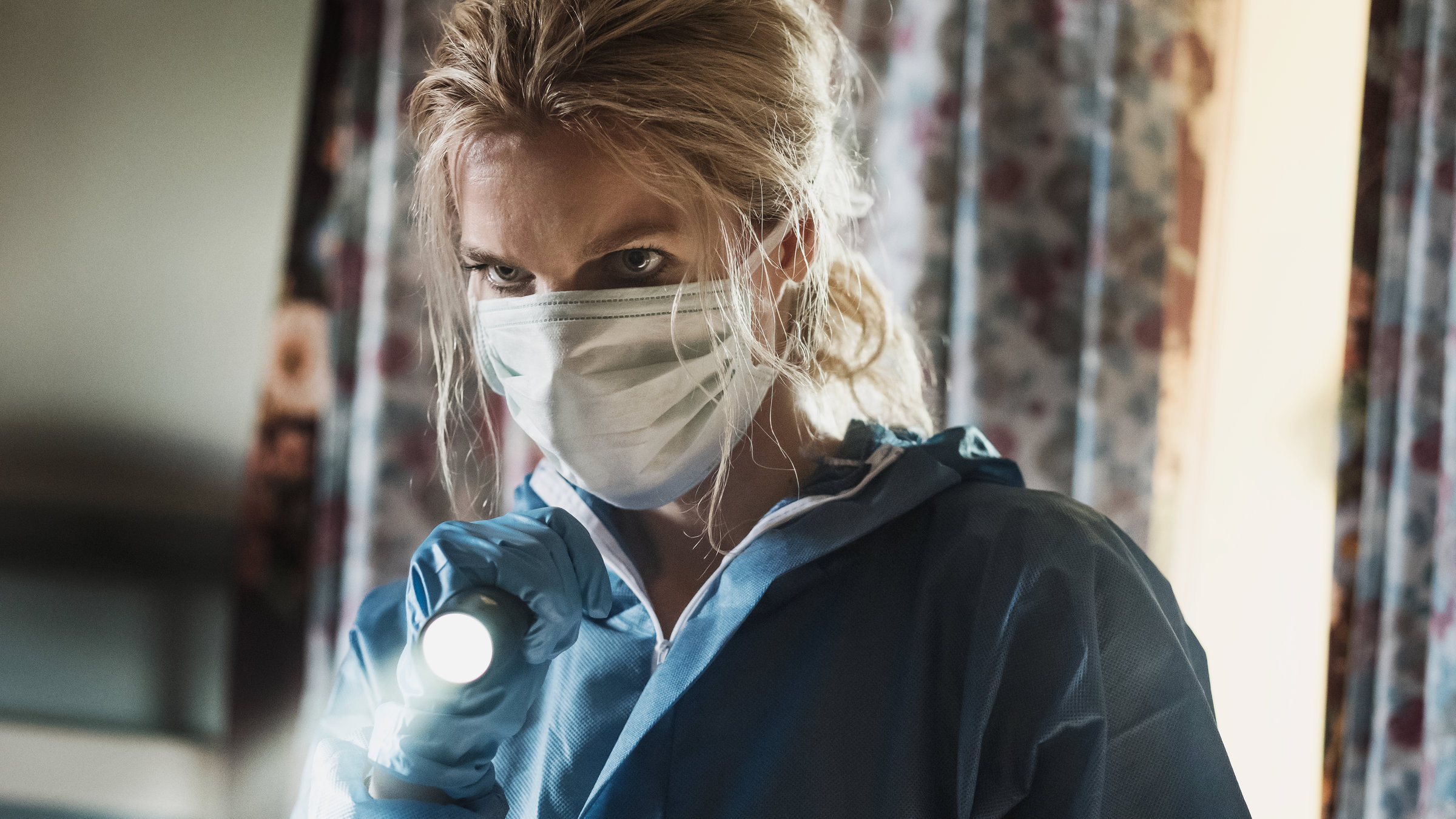 "The Team II (1)": Nelly (Marie Bach Hansen) läuft mit einer Taschenlampe durch die Räume der Marschfarm. Sie trägt einen Mundschutz und einen blauen Overall.