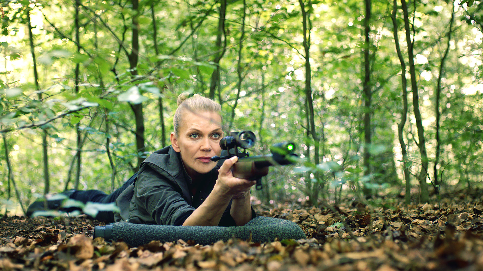 "Helen Dorn - Das Recht zu schweigen": Helen Dorn (Anna Loos) liegt bäuchlings mit einem Gewehr im Anschlag auf dem Waldboden.