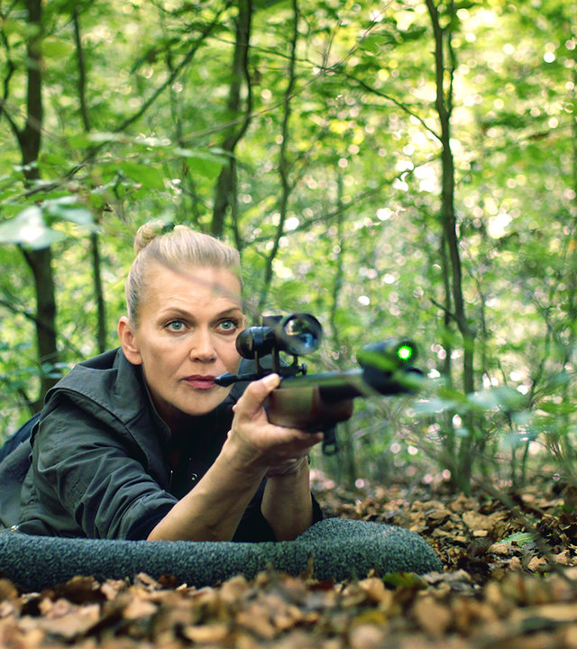 "Helen Dorn - Das Recht zu schweigen": Helen Dorn (Anna Loos) liegt bäuchlings mit einem Gewehr im Anschlag auf dem Waldboden.