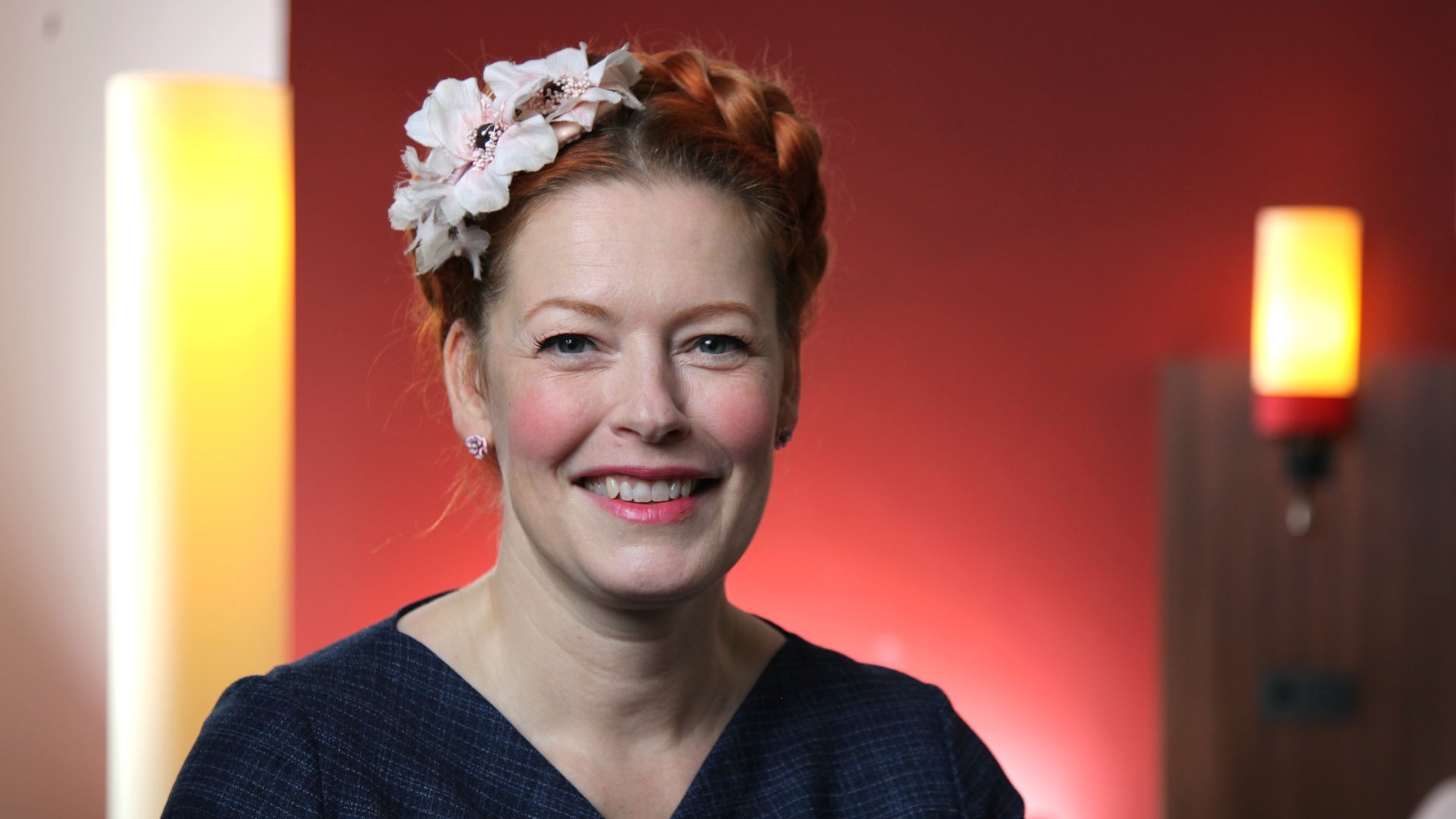 "ZDF-History: Mythos Kaufhaus - Shoppen damals und heute". Enie van de Meiklokjes steht mit Blumen im Haar vor einer roten Wand.