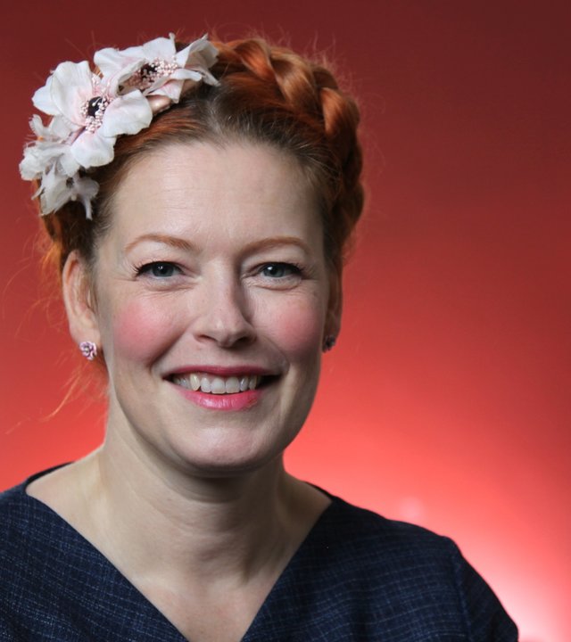 "ZDF-History: Mythos Kaufhaus - Shoppen damals und heute". Enie van de Meiklokjes steht mit Blumen im Haar vor einer roten Wand.