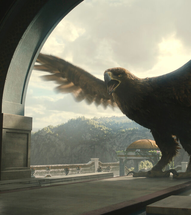 "Der Herr der Ringe: Die Ringe der Macht - Der Adler und das Zepter": Ein riesiger Adler steht mit ausgebreiteten Schwingen in einem Torbogen. Hinter ihm sind draußen die Hügel von Númenor zu erkennen. Dem Adler gegenüber steht Ar-Pharazôn (Trystan Gravelle) in einem Saal. Er ist nur von hinten zu sehen.
