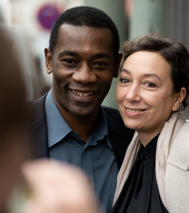"Le Prince": Joseph (Passi Balende) und Monika (Ursula Strauss) stehen eng nebeneinander und lächeln in die Kamera, mit der jemand sie fotografiert.