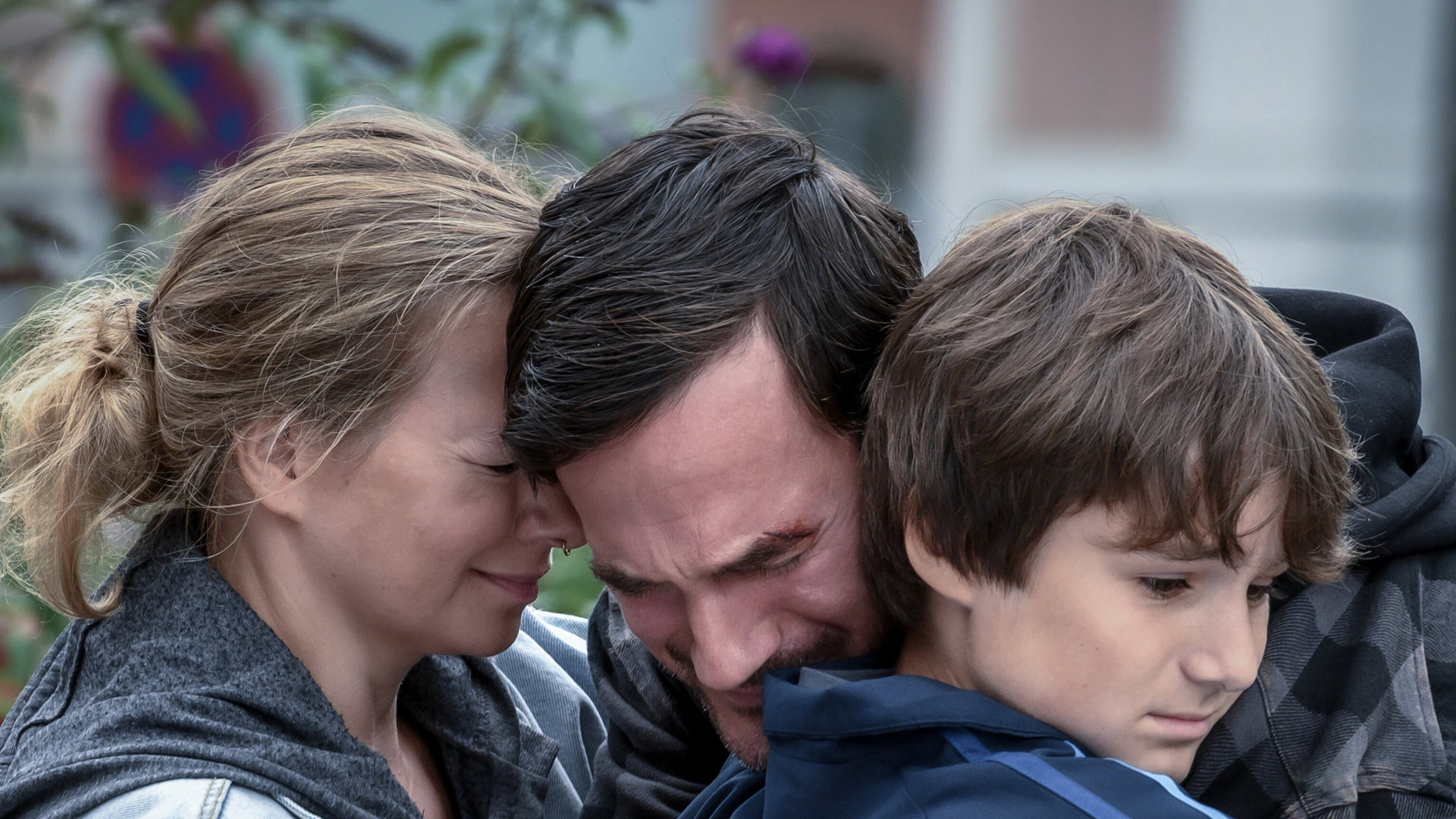 "SOKO Linz - Kältestarre": Anselm Kramer und (Sönke Möhring) und seine Kinder Julian (Leopold Pallua) und Sinia (Angelika Strabsen) liegen sich trauernd in den Armen. Sinia hält einen Plüsch-Tiger in der Hand.