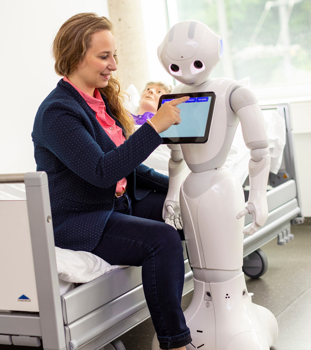 "37°: Schlauer als der Rest der Welt - Hochbegabte im Alltag": Pia Beyer-Wunsch mit dem Roboter Pepper, den sie im Rahmen ihrer Doktorarbeit entwickelt, in der Universität Ulm mit einem Patienten-Dummie im Hintergrund im Bett.