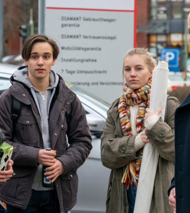 "Letzte Spur Berlin - Klimaangst": Finn Berger (Louie Betton), Daniel (Malik Blumenthal), Elli (Louise Sophie Arnold) und Jens Ehrenberg (Lukas Turtur) stehen vor einem Autohaus. Elli hält ein aufgerolltes Banner in der Hand, Finn eine Bierflasche.
