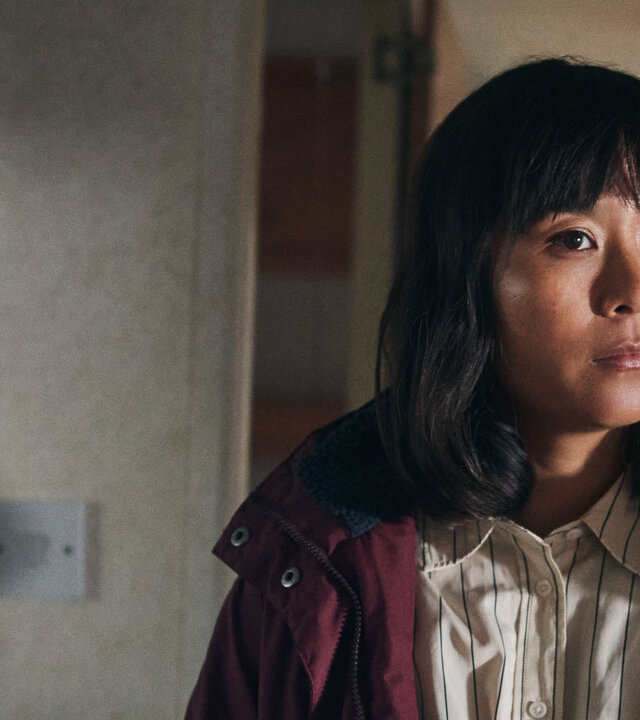 "Under Salt Marsh - Tod in den Salzwiesen - Die schwarze Sau": Jess (Naomi Yang) steht in einem Raum. Sie trÃ¤gt einen Mantel und blickt nach vorne.