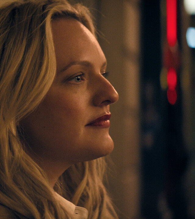 "The Veil - Kein Zurück": Imogen Salter (Elisabeth Moss) steht im Dunkeln vor einer Hauswand. Im Hintergrund sind verschwommene Lichter zu sehen.