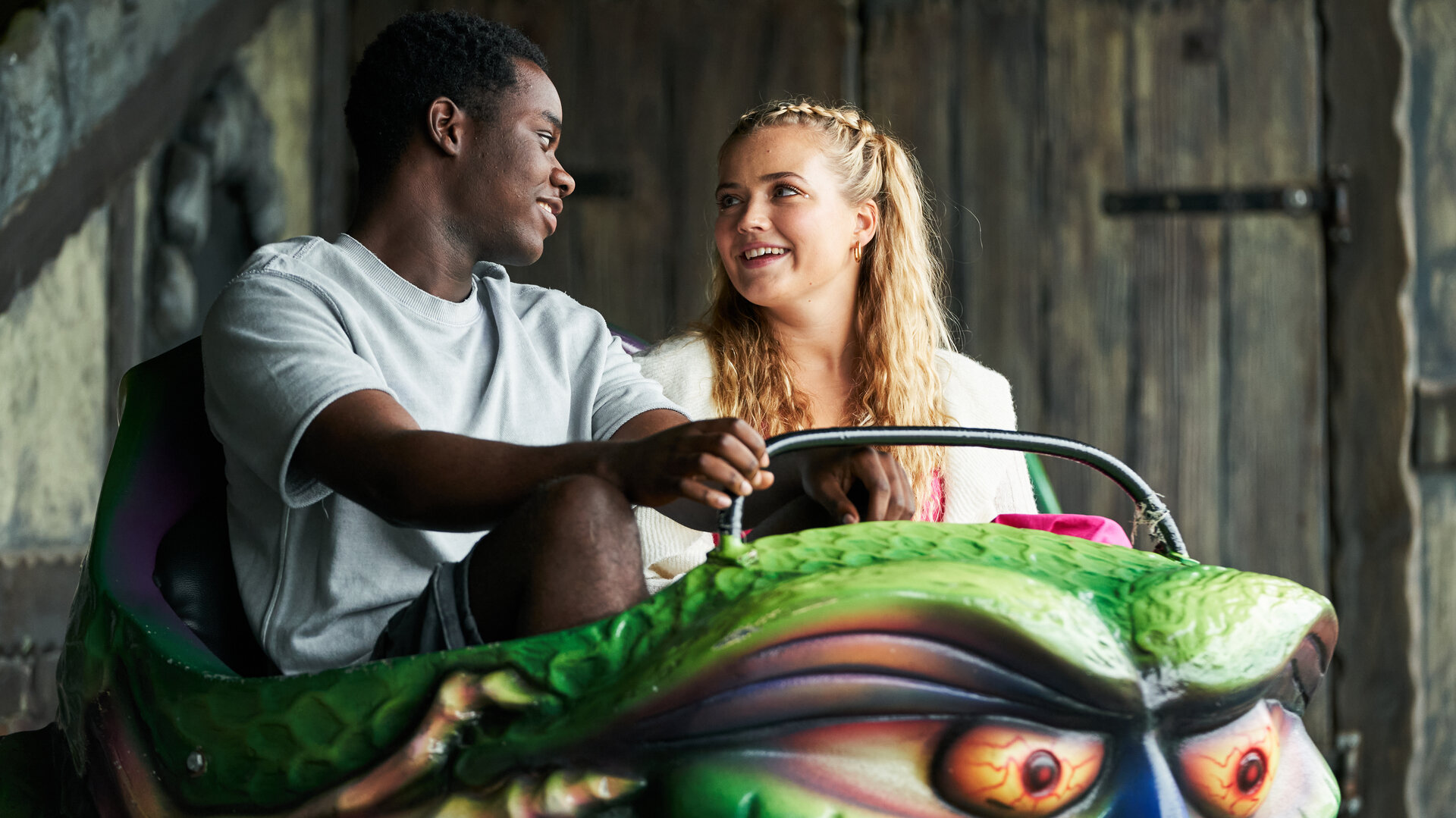 "Boarders - Welcome to St. Gilbert's - Secrets & Surprises": Jaheim (Josh Tedeku) und Florence (Rosie Graham) sitzen in der Gondel einer Geisterbahn. Die beiden schauen sich lächelnd an.
