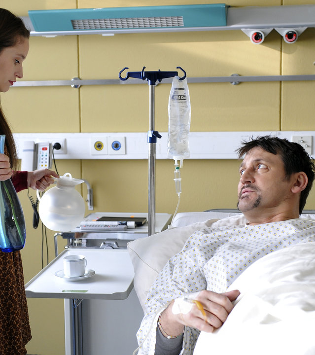 "Notruf Hafenkante - Hunger auf Blut": Nadja (Lea Draeger) kümmert sich liebevoll um ihren Freund, den Bestsellerautoren Enno Krohn (Ingo Naujoks), der im Krankenhaus liegt. Sie steht mit einer Blue und einer Kaffeekanne an seinem Bett.