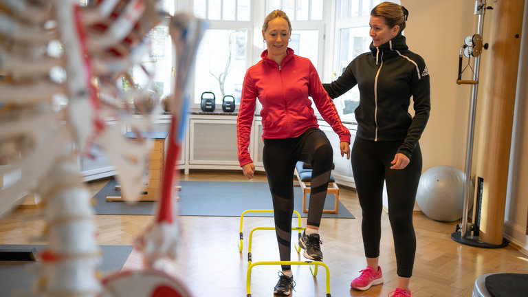 "37° Späte Diagnose mit Folgen - Nina kämpft sich zurück ins Leben": Nina, im roten Oberteil, hebt das Bein. Eine Frau (rechts im Bild) im schwarzen Oberteil hält unterstützend den Arm.