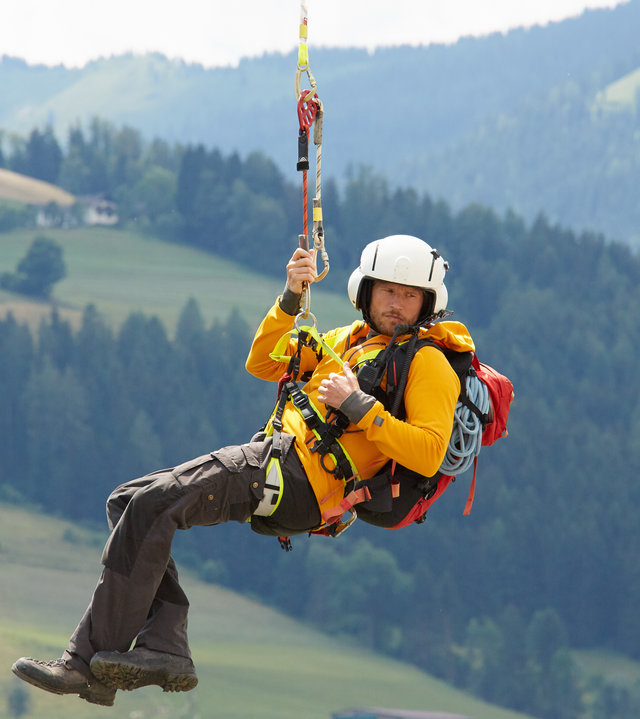 "Die Bergretter: Wiedersehen (1)": Bergretter Markus (Sebastian Ströbel) hängt an der Rettungsleine unter dem Helikopter und schwebt über die Landschaft.