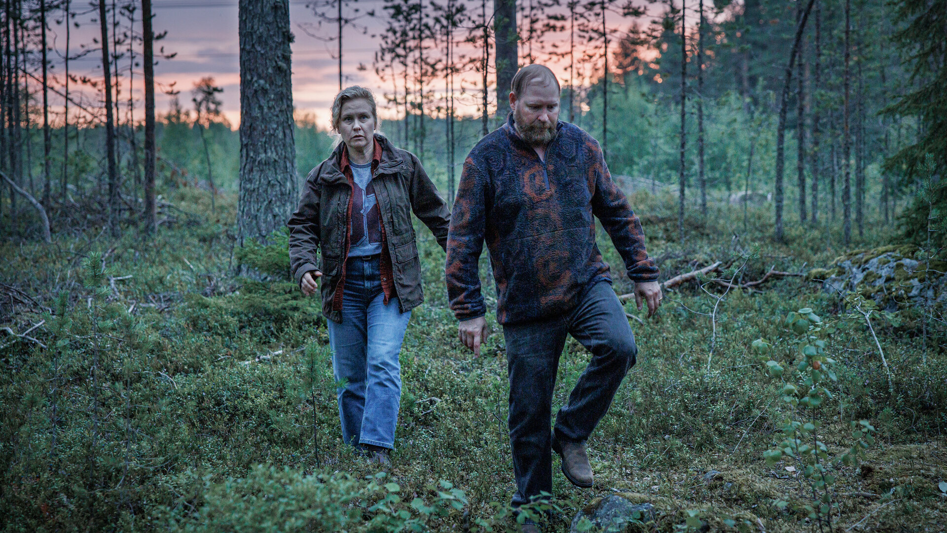 "Wolfssommer – Blutige Spuren - Wer bist du?": Hannah (Eva Melander) und Thomas (Henrik Dorsin) laufen in der Dämmerung über eine Lichtung im Wald.