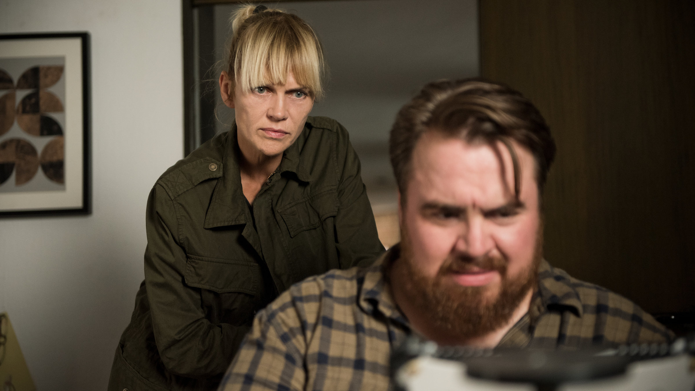 "Helen Dorn - Atemlos": Weyer (Tristan Seith) sitzt an einem Tisch und schaut konzentriert vor sich. Helen Dorn (Anna Loos) steht hinter ihm und schaut in die gleiche Richtung.