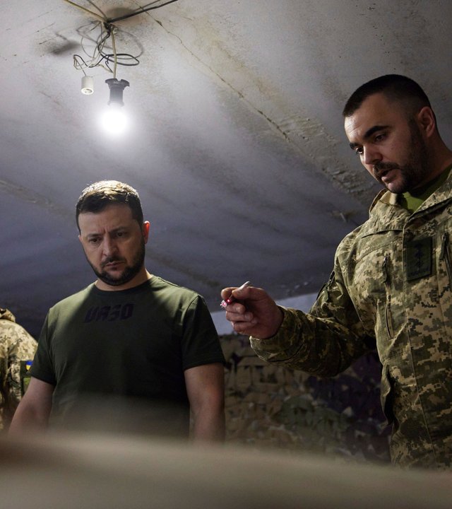 "Tatort Ukraine - Selenskyj": Drei Männer, in der Mitte der ukrainische Präsident Wolodymyr Selenskyj, die zwei anderen in Militäruniform stehen in einem unterirdischen Raum und blicken nach unten.