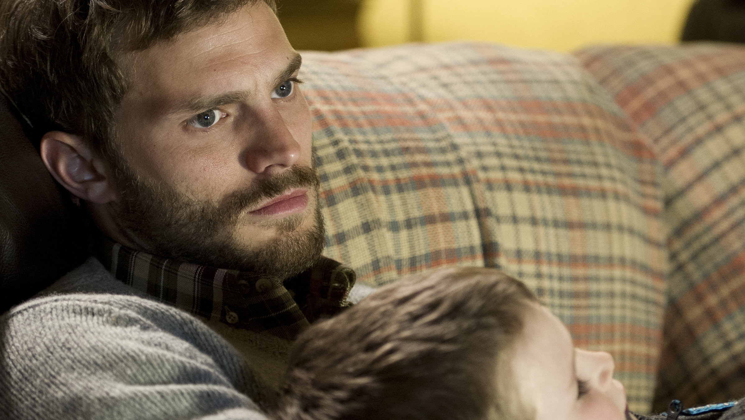 "The Fall - Tod in Belfast (2)": Paul Spector (Jamie Dornan) liegt mit seinem Sohn Liam (David Beatie) auf dem Sofa. Paul sieht nachdenklich aus.