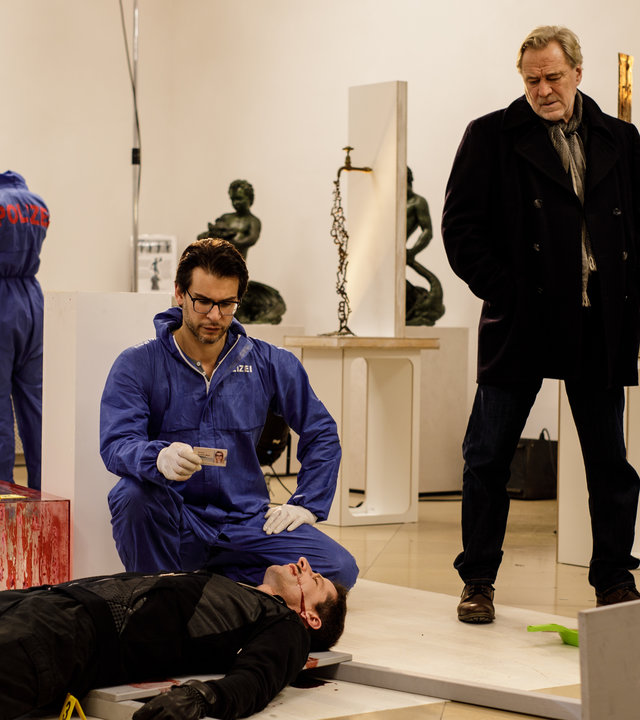 "SOKO München - Nachtwache": Am Tatort in einem Museum liegt eine Leiche am Boden , Dr. Weissenböck (Florian Odendahl) sitzt in der Hocke daneben und schaut sich den Ausweis der Leiche an. Rechts von der Leiche steht Antonia Bischoff (Amanda da Gloria), rechts steht Arthur Bauer (Gerd Silberbauer) neben ihm steht Jean-Claude (Sebastian Griegel) ein Angestellter des Museum.