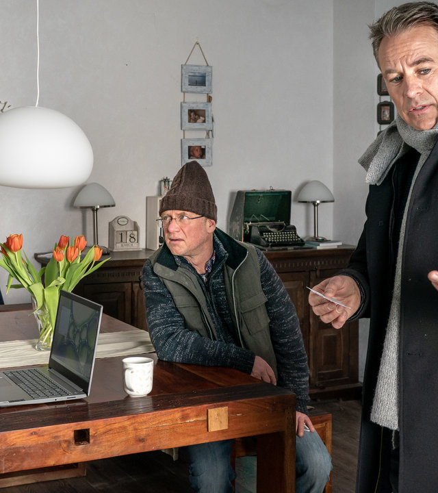 "SOKO Leipzig - Trautes Heim, Glück allein": Vera Höhne (Muriel Baumeister) steht in ihrem Wohnzimmer vor dem Esstisch auf dem ein Laptop steht. Ulf Höhne (Rainer Strecker) sitzt ihr gegenüber. Jan Maybach (Marco Girnth) spricht mit dem Ehepaar Höhne und blickt dabei in Richtung Kamera.