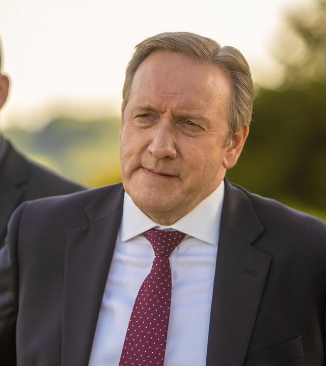 "Inspector Barnaby: Mord ist keine Hexerei": DS Jamie Winter (Nick Hendrix) und DCI John Barnaby (Neil Dudgeon) stehen in Anzügen gekleidet nebeneinander im Freien und schauen ernst nach links aus dem Bild.