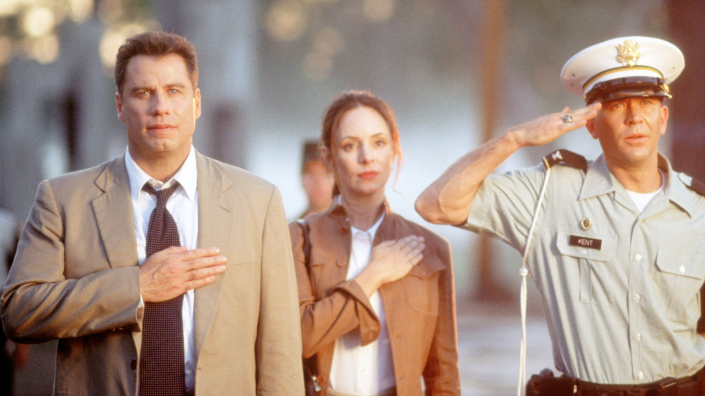 "Wehrlos - Die Tochter des Generals": Paul Brenner (John Travolta) und Sara Sunhill (Madeleine Stowe) legen symbolisch ihre rechte Hand auf das Herz. Colonel Kent (Timothy Hutton) steht mit angewinkeltem Arm daneben und salutiert.