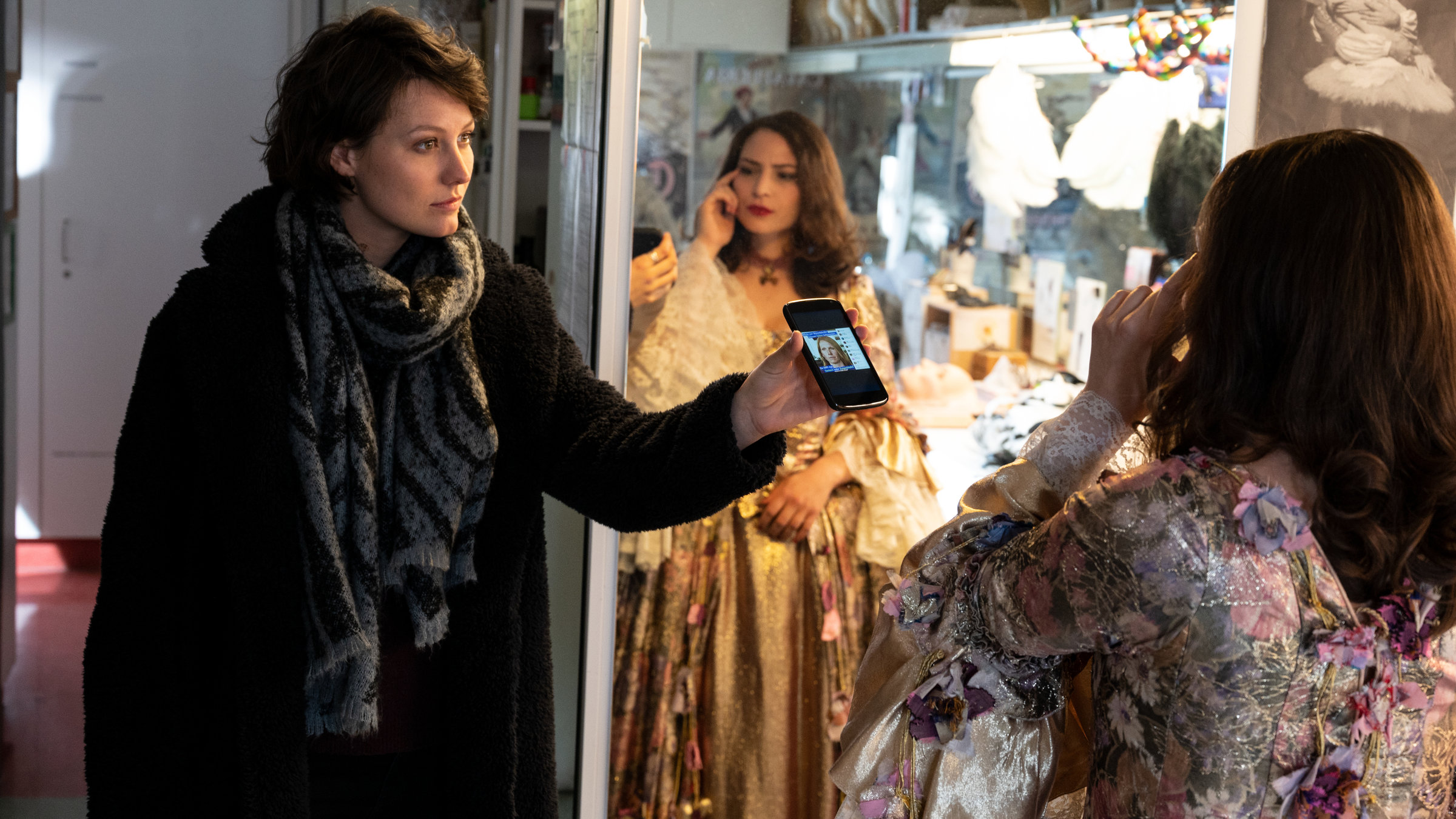 "SOKO Stuttgart – Der letzte Akt": Die Kommissarin Nele Becker (Nina Siewert) befragt in einem Kostümraum der Oper die Opernsängerin Irina Komarow (Rebecca Lara Müller). Diese steht in einem ausladenden Bühnenkostüm vor dem Spiegel und macht eine nachdenkliche Geste. Nele Becker hält ihr ein Handy entgegen, auf dem das Foto des Opfers zu sehen ist, und schaut Komarow erwartungsvoll an.