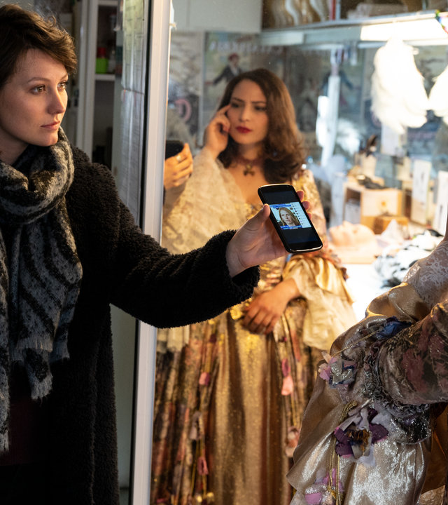 "SOKO Stuttgart – Der letzte Akt": Die Kommissarin Nele Becker (Nina Siewert) befragt in einem Kostümraum der Oper die Opernsängerin Irina Komarow (Rebecca Lara Müller). Diese steht in einem ausladenden Bühnenkostüm vor dem Spiegel und macht eine nachdenkliche Geste. Nele Becker hält ihr ein Handy entgegen, auf dem das Foto des Opfers zu sehen ist, und schaut Komarow erwartungsvoll an.