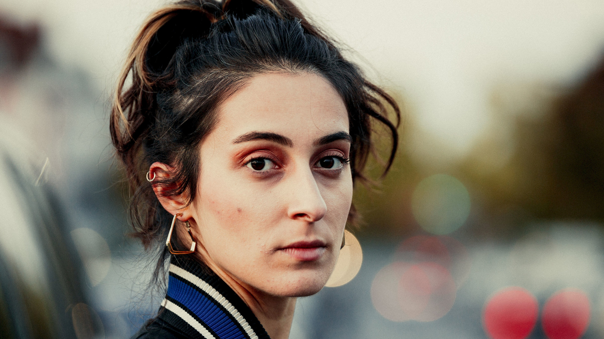 "Ansonsten geht's mir gut": Porträtaufnahme einer jungen Frau, die in die Kamera blickt, im Hintergrund verschwommen die Rücklichter von Autos.