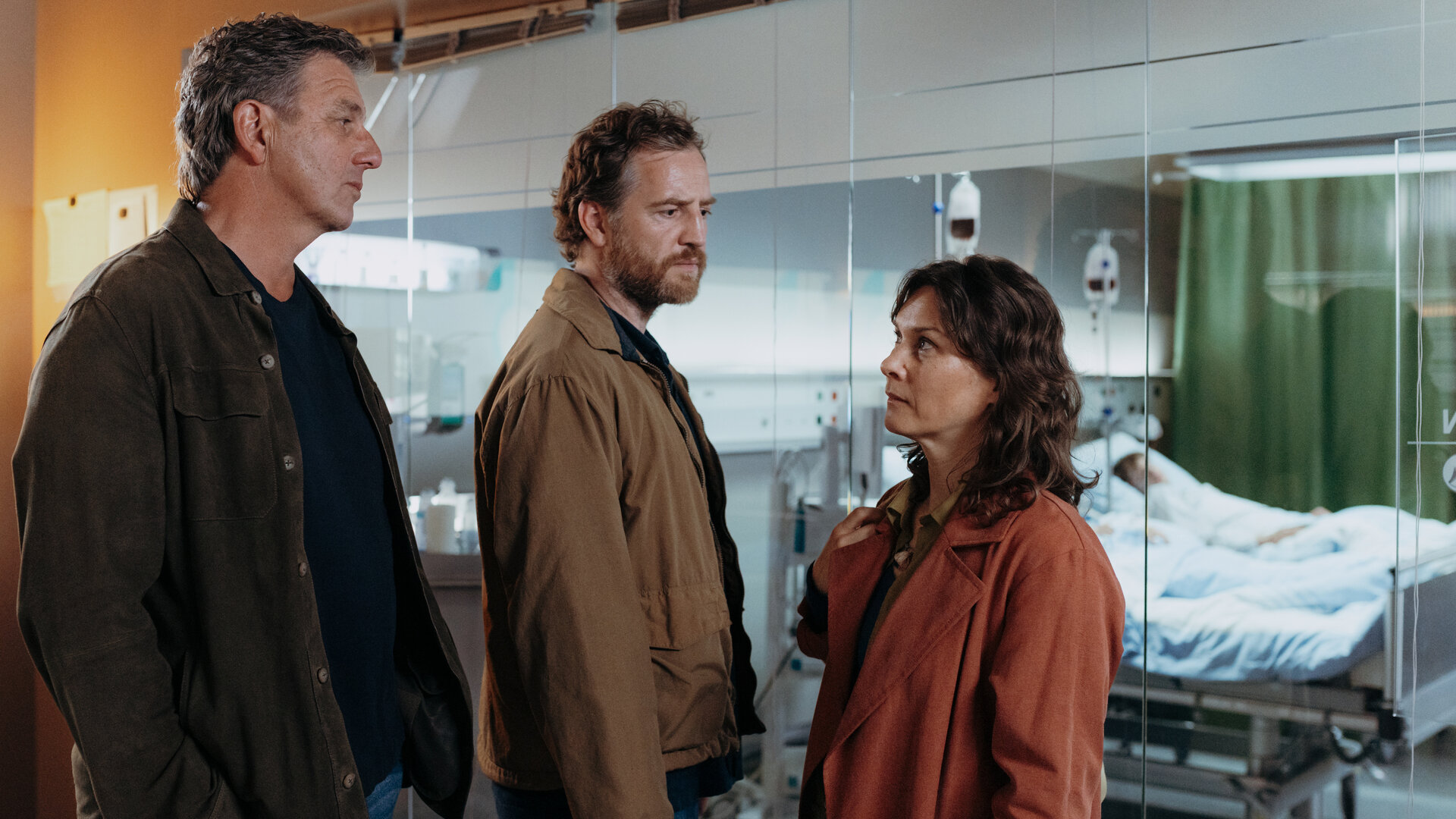 "Der Bergdoktor: Neuanfänge": In der Klinik: Dr. Martin Gruber (Hans Sigl) steht mit Clara Meindl (Kathrin von Steinburg) und Jakob Meindl (Tom Radisch) vor dem Krankenzimmer ihrer Kinder Mia Meindl (Finja Leonie Meyer) und Noah Meindl (Levi Brandl). Besorgt schauen sich Dr. Gruber und Clara Meindl an, während Jakob Meindl traurig vor sich hin blickt. Beide Kinder liegen mit Infusionen in den Betten.