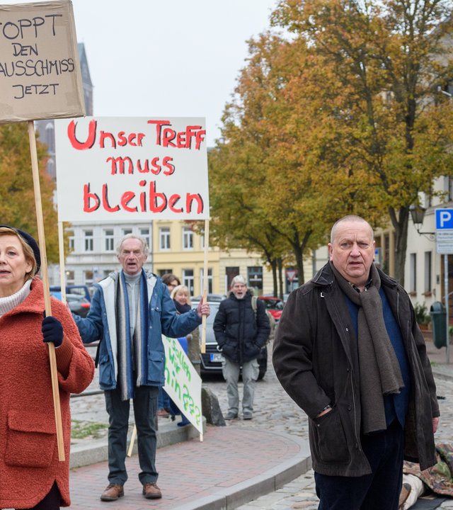 "SOKO Wismar – Hemingways Bauch": Auf einer Straße in der Wismarer Innenstadt blockieren Marlies Plattke (Judith von Radetzky) und weitere Demonstrierende die Durchfahrt. Paula Moorkamp (Stella Hinrichs) und Jan Reuter (Udo Kroschwald) stehen auf der Straße. Holger Nowak (Till Demuth) fotografiert die Demonstration.