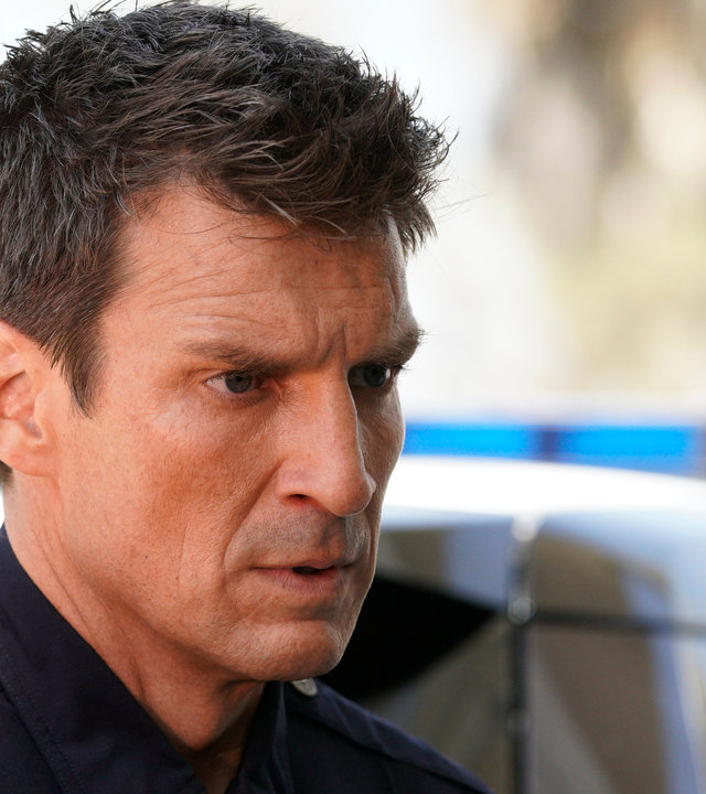 "The Rookie - Nachtschatten": John Nolan (Nathan Fillion) schaut mit entschlossenem Blick in die Ferne. Im Hintergrund ist ein Polizeiauto zu sehen.