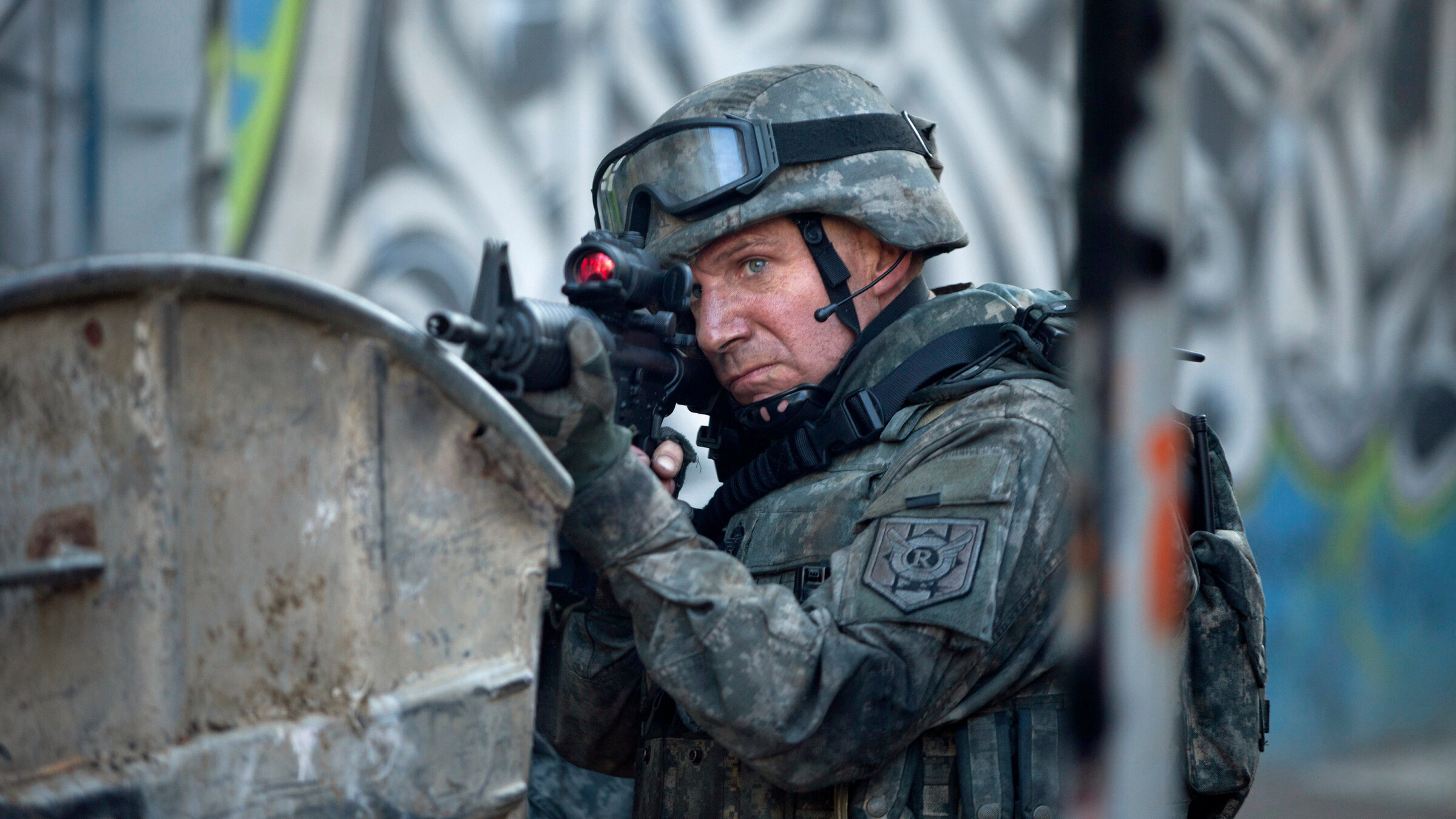 „Coriolanus“: In martialischer moderner Kampfmontur inklusive Helm zielt General Coriolanus (Ralph Fiennes) mit einem Gewehr konzentriert und entschlossen auf ein Ziel außerhalb des Bildes.