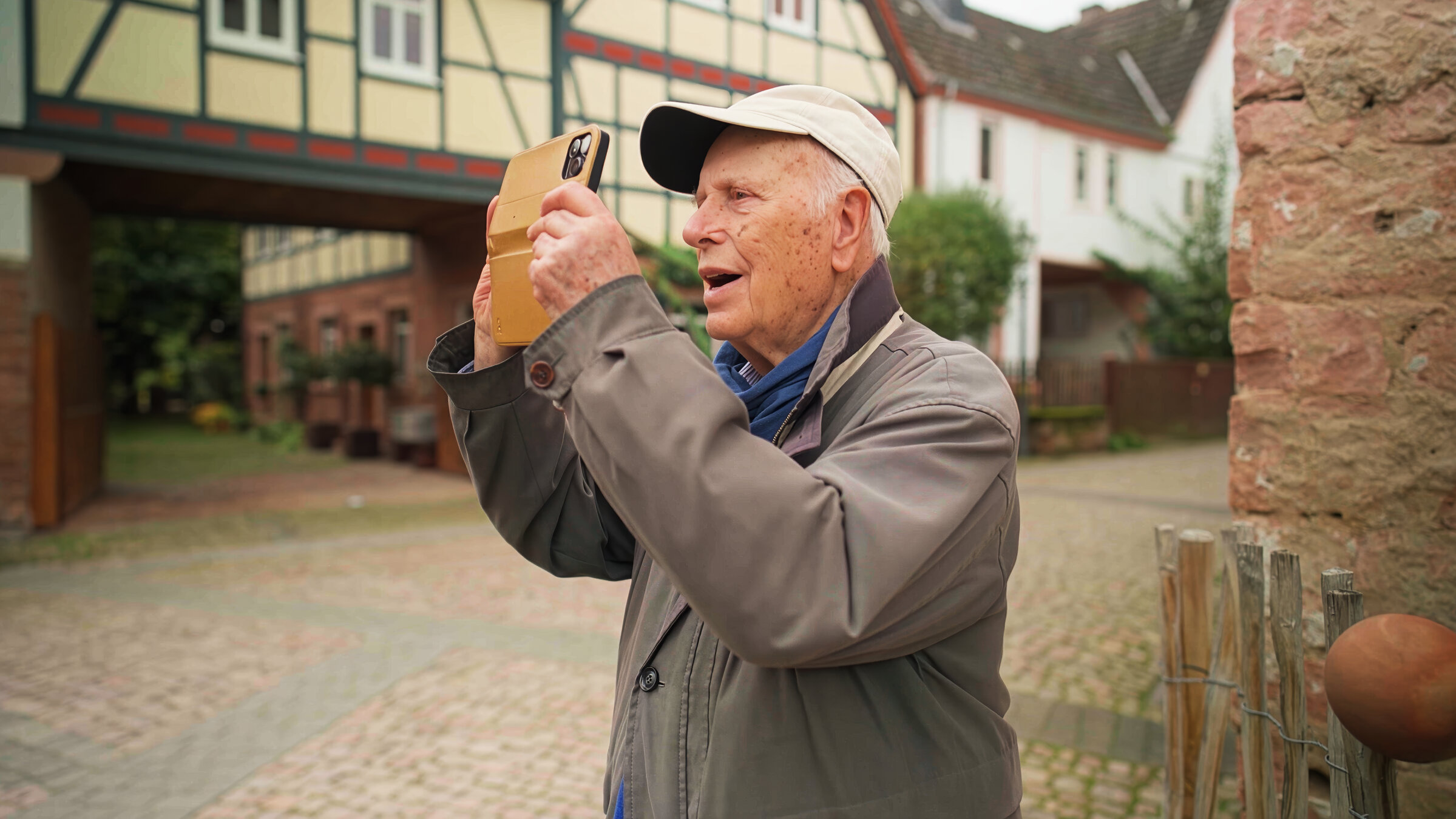 "100 Jahre Leben: was wirklich zählt": Helmut steht vor Fachwerkhäusern und macht mit seinem Smartphone ein Foto.