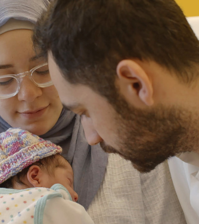 "37°: Guter Hoffnung - Eltern werden in drei Religionen": Ein junges Paar schaut zärtlich auf sein kleines Baby. Die Frau hält das Baby in den Armen, sie trägt Brille und Kopftuch. Das Baby eine bunte Wollmütze.