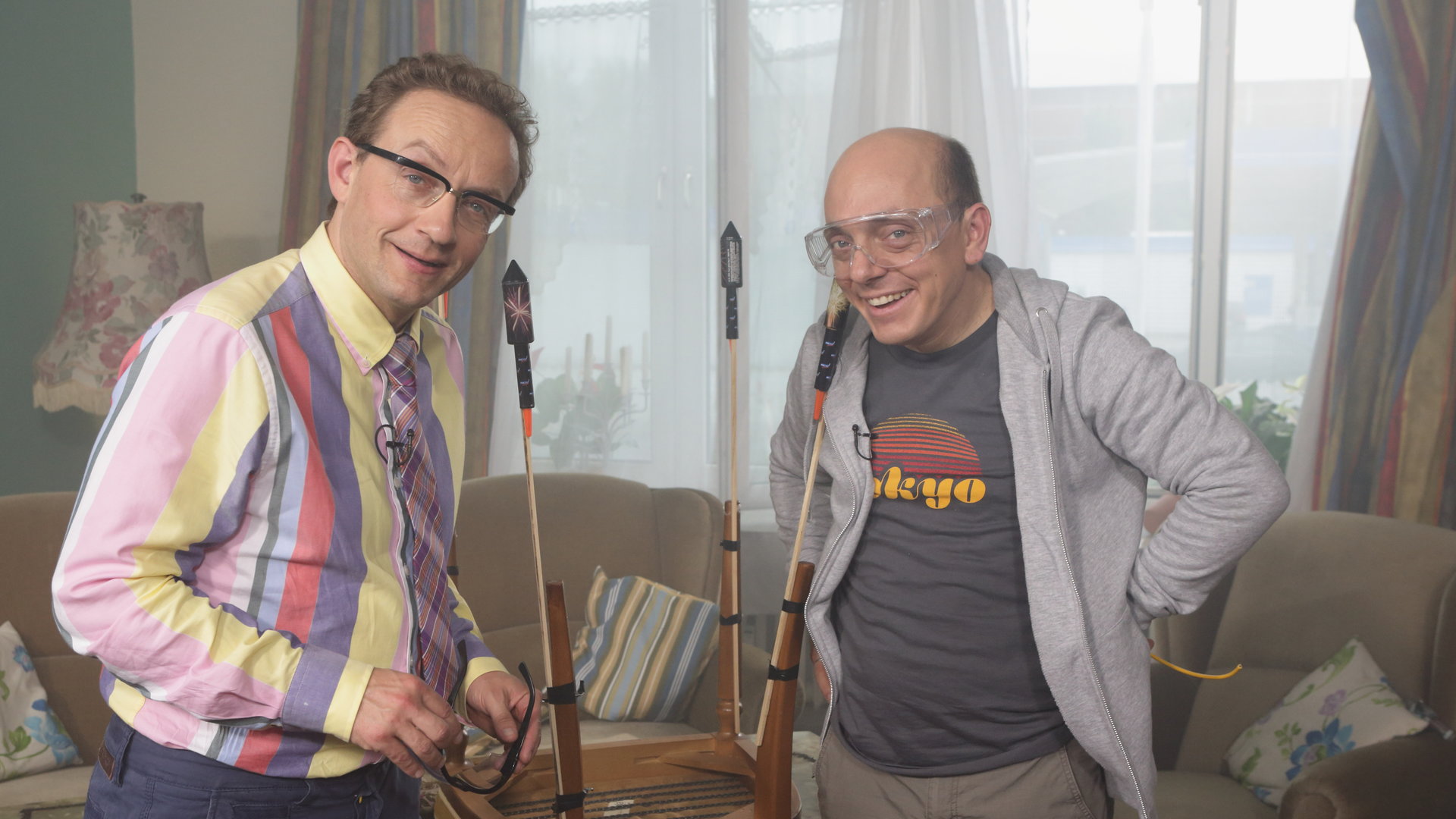 "Nicht nachmachen!": Wigald Boning und Bernhard Hoëcker stehen in einem Wohnzimmer und binden Sylvester-Knaller an Stuhlbeine.