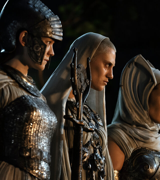 "Der Herr der Ringe: Die Ringe der Macht - Das Auge": Die drei Mystikerinnen (Edith Poor, Bridie Sisson, Kali Kopae) stehen nebeneinander im Dunkeln und beobachten etwas. Eine von ihnen trägt einen Helm, die anderen beiden Kopftücher.