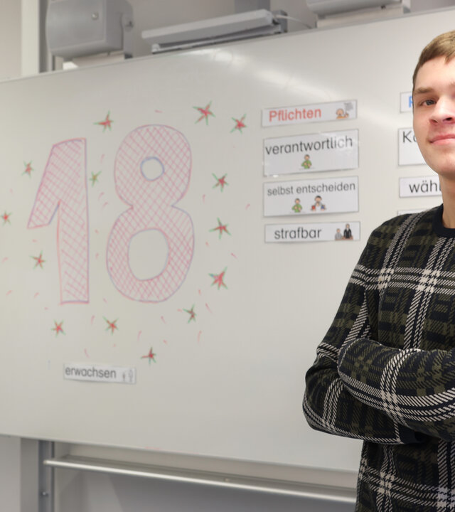 "einfach Mensch - Christopher Bahr: Was ändert sich in meinem Leben?": Christopher Bahr aus Erlangen steht in einem Seminarraum vor einer Tafel. Auf der Tafel steht "18".