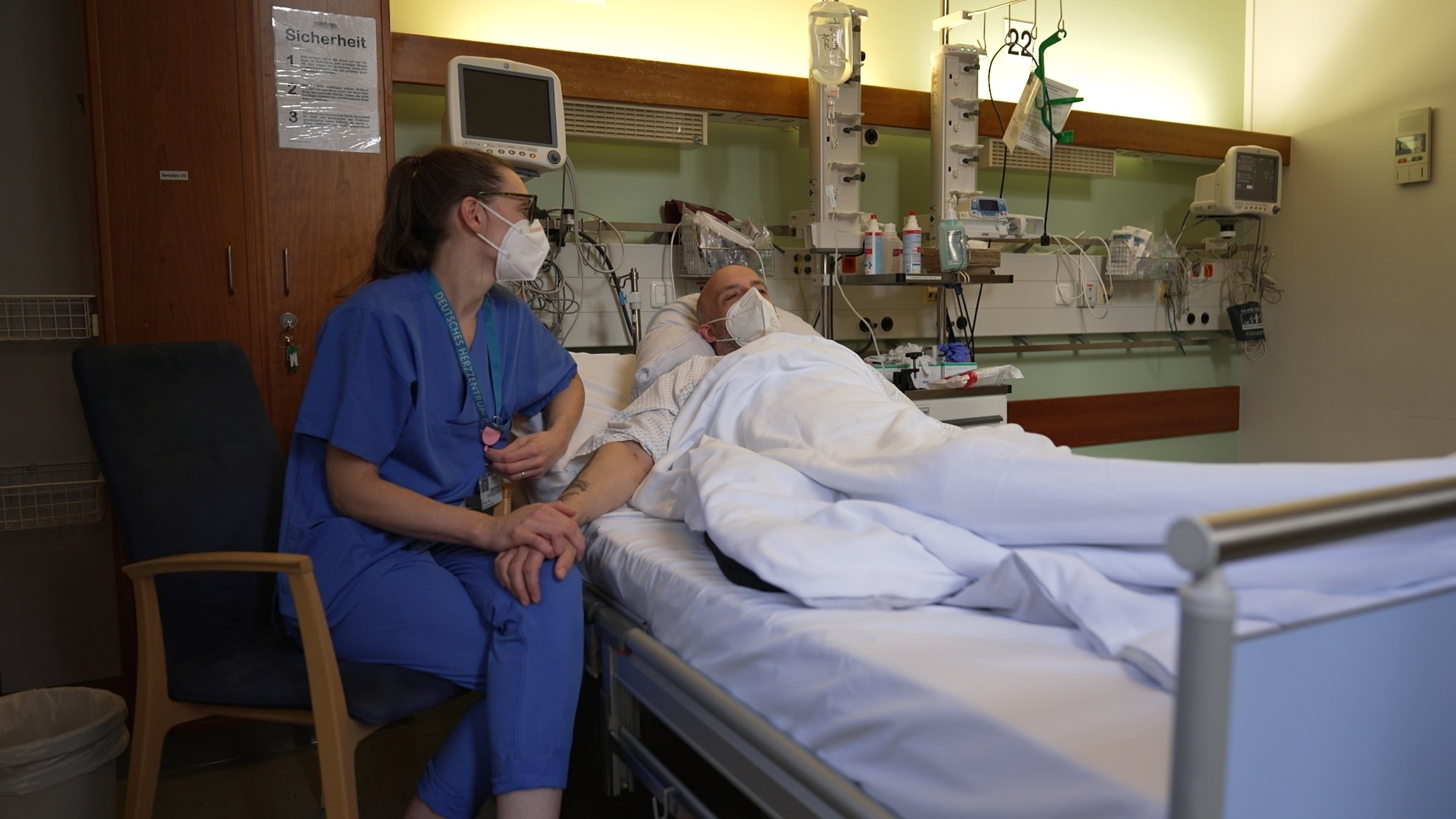 "37° Dein Herz in mir - Organspende als zweite Chance": Dirk liegt in einem Krankenhausbett. Links neben ihm sitzt seine Freundin auf einem Stuhl. Sie trägt blaue Krankenhauskleidung. Gemeinsam warten die Beiden auf seine Operation.