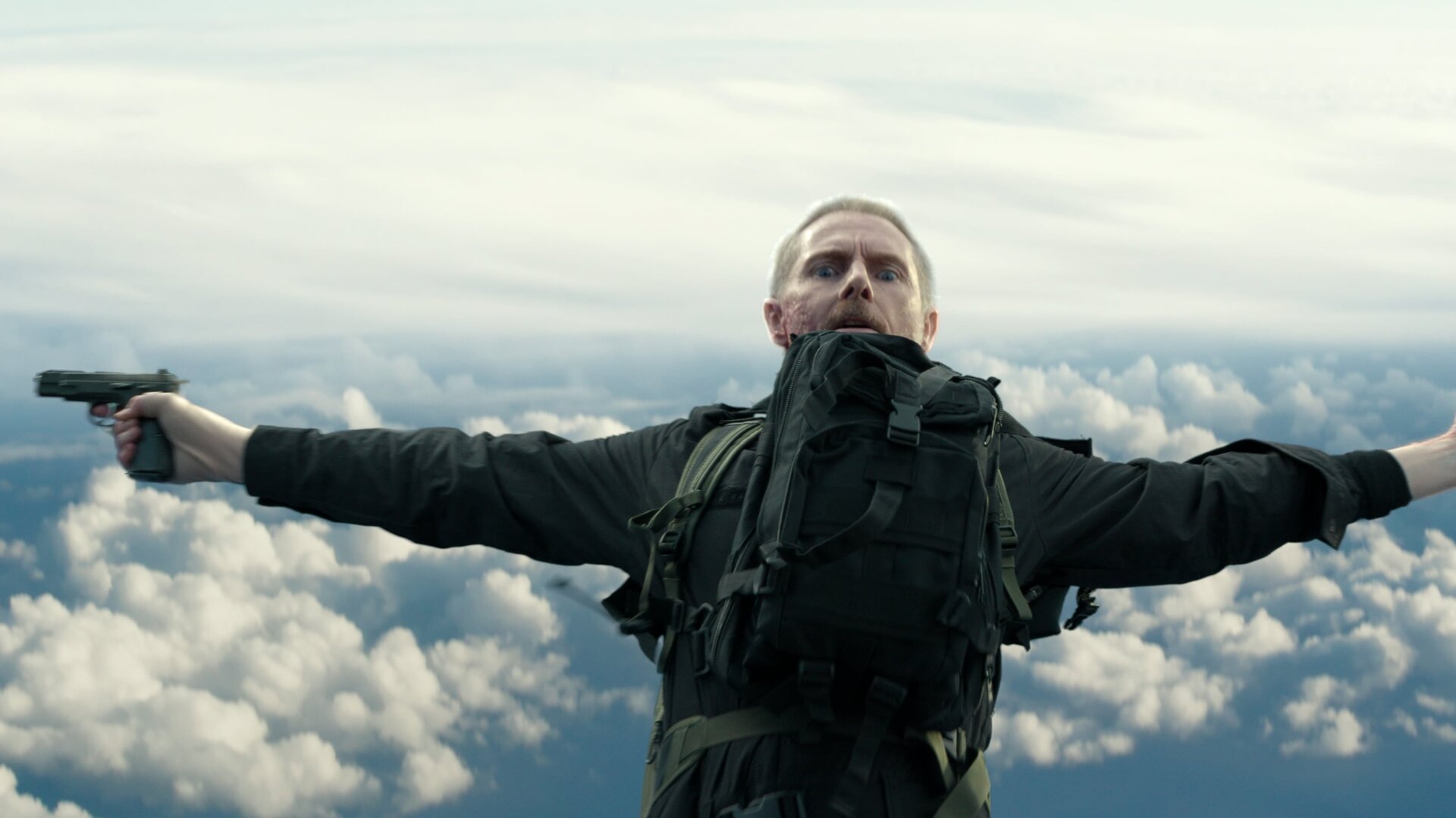 "Paris Has Fallen - Blindflug": Pearce (Sean Harris) breitet die Arme aus und lässt sich nach hinten, in den bewölkten Himmel fallen. In der rechten Hand hält er eine Pistole.