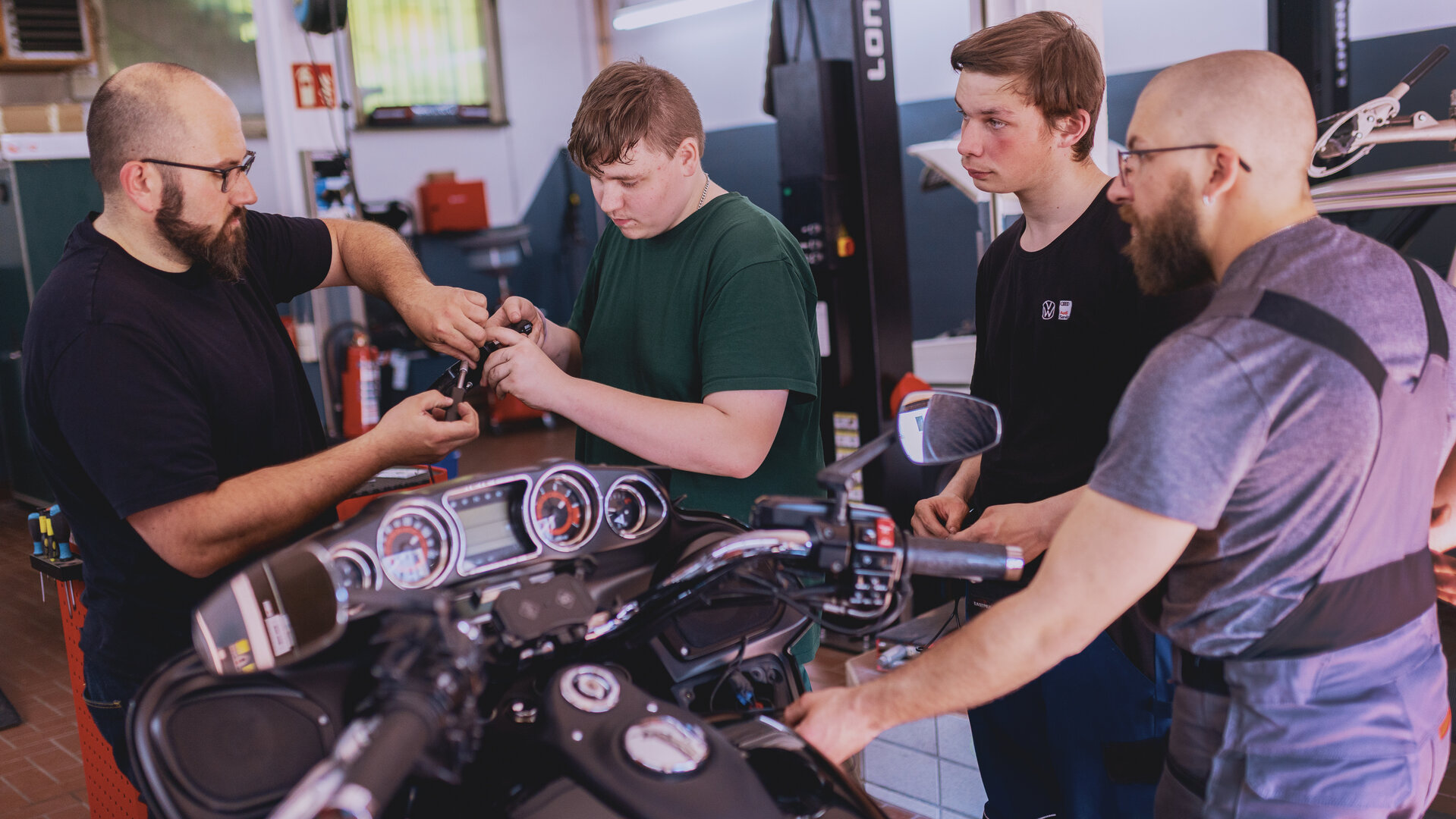 "Aktion Mensch - Glückszahlen der Woche": Vier Männer stehen in einer Werkhalle um einem Motorrad herum.