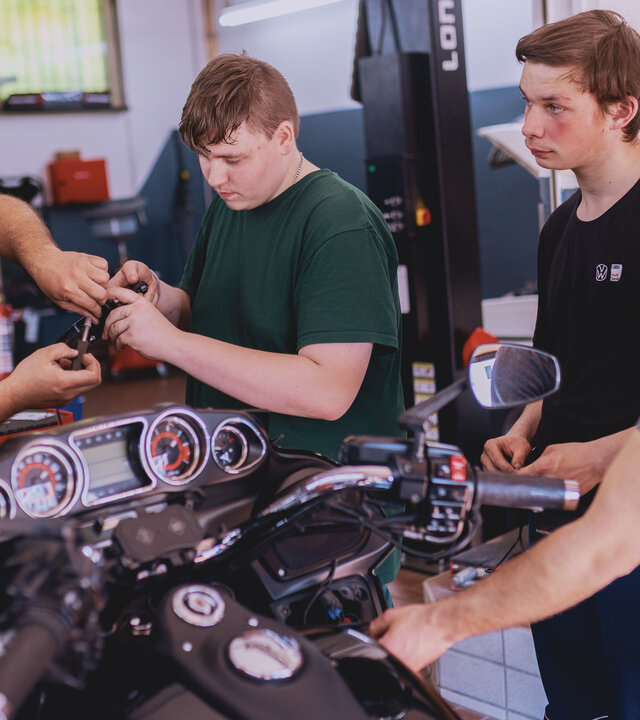 "Aktion Mensch - Glückszahlen der Woche": Vier Männer stehen in einer Werkhalle um einem Motorrad herum.