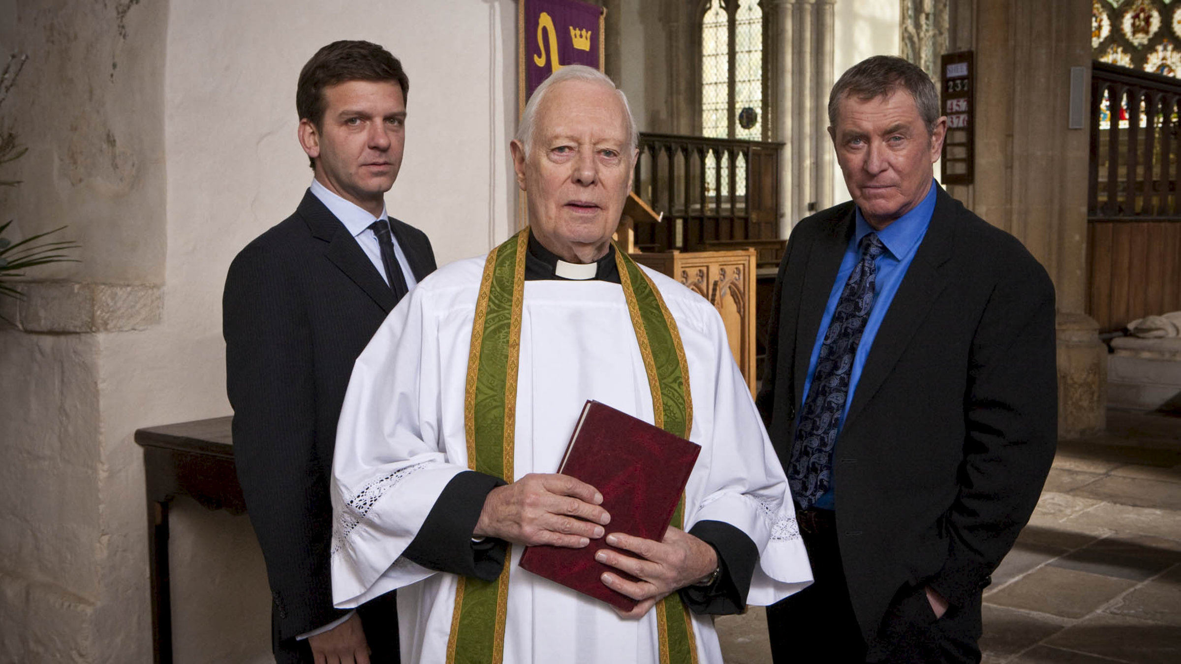 "Inspector Barnaby - Mord von Meisterhand": DS Ben Jones (Jason Hughes), Reverend Gregory (Clifford Rose) und DCI Tom Barnaby (John Nettles) stehen nebeneinander in der Kirche und schauen in die Kamera.